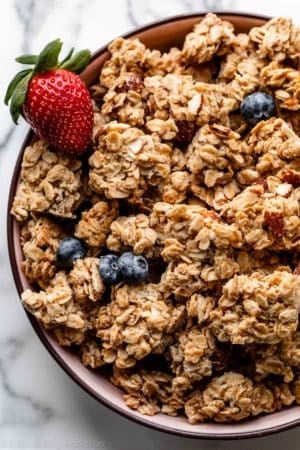 granola clusters in pink bowl with strawberry and blueberries.