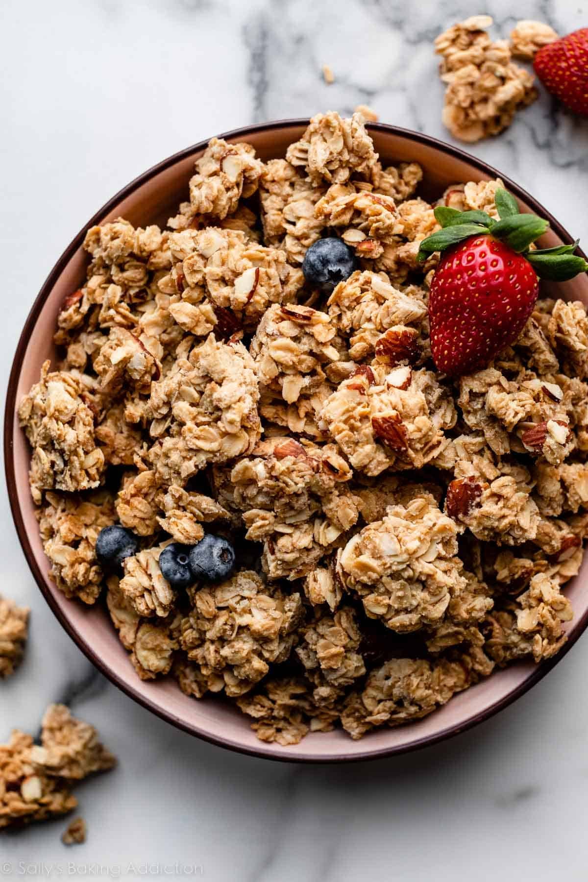 clusters of granola in pink bowl with strawberry and blueberries.