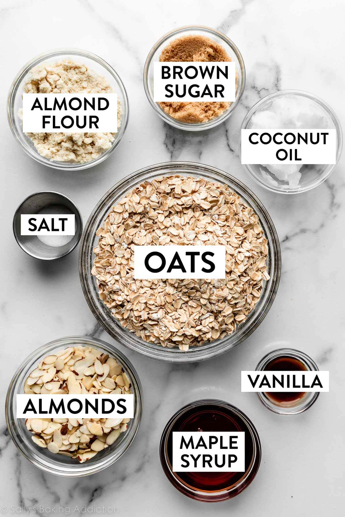 ingredients measured on marble counter including oats, brown sugar, coconut oil, almond flour, and maple syrup.