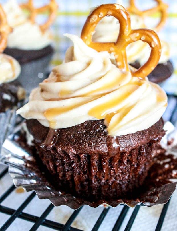 chocolate cupcakes topped with salted caramel frosting and a pretzel on a cooling rack