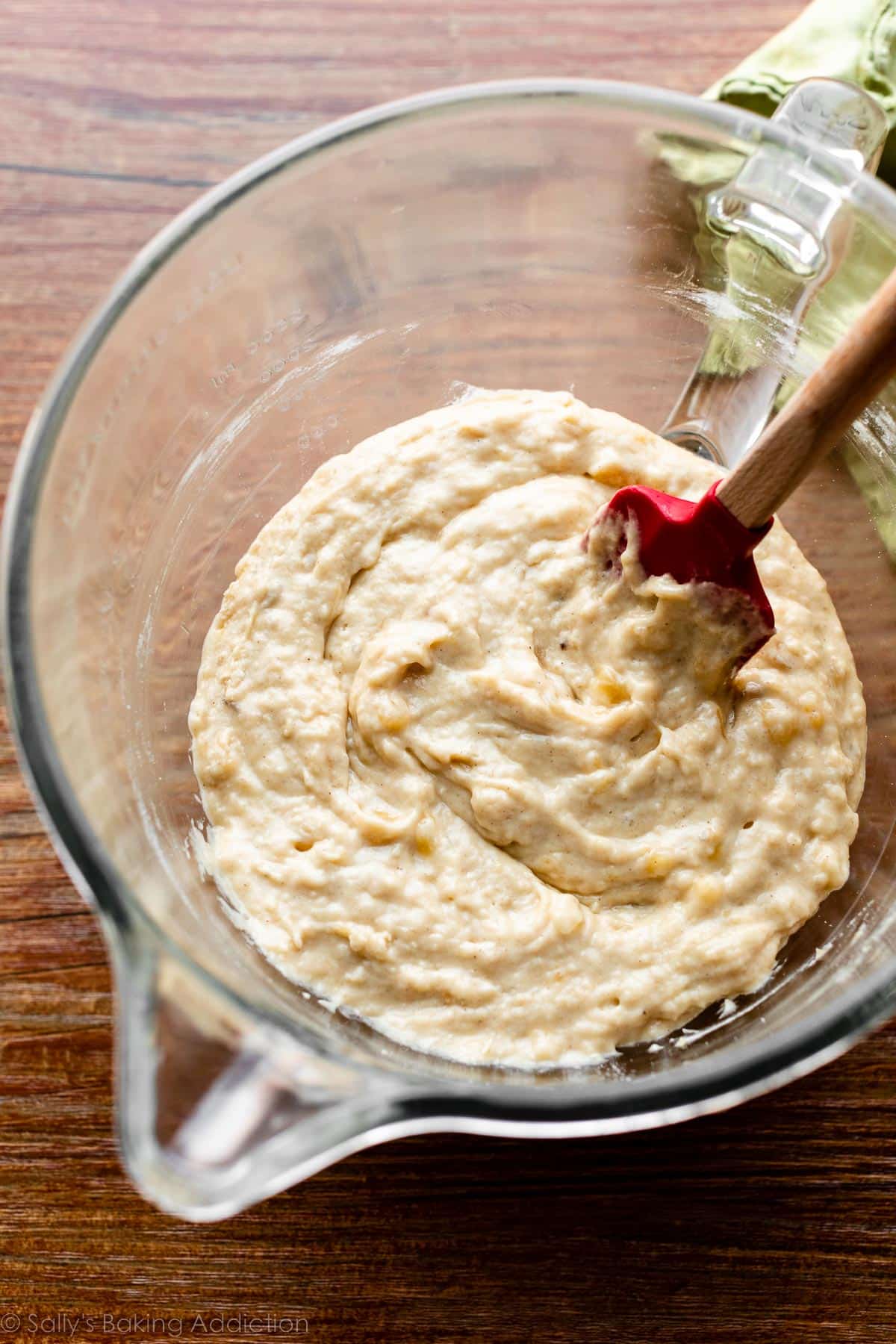 yellow bread batter in glass mixing bowl with red rubber spatula.