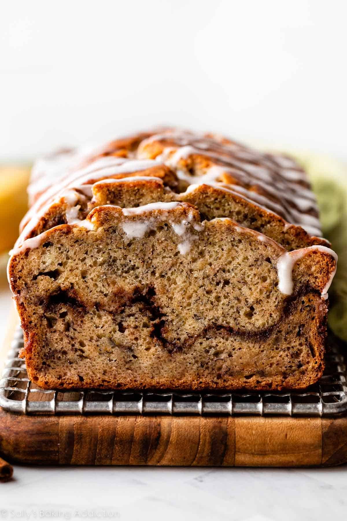 banana bread slice with cinnamon swirl and vanilla icing on top sitting on wire rack on cutting board.