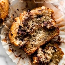 banana chocolate chip cinnamon streusel muffin cut open sitting in muffin wrapper.