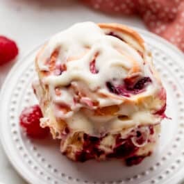 raspberry sweet roll with cream cheese icing on white plate.