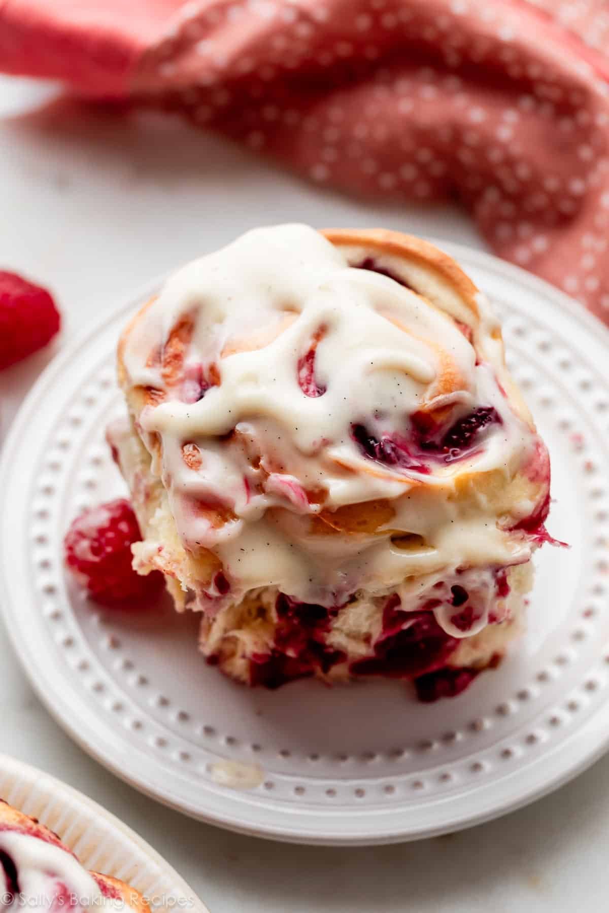 raspberry sweet roll with cream cheese icing on white plate.