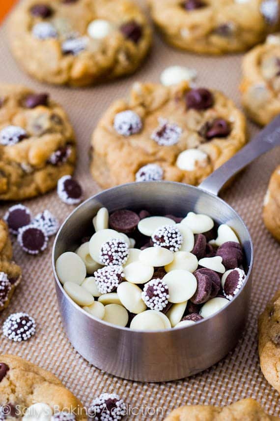 triple chocolate chip cookies on a silpat baking mat with a measuring cup full of triple chocolate chips