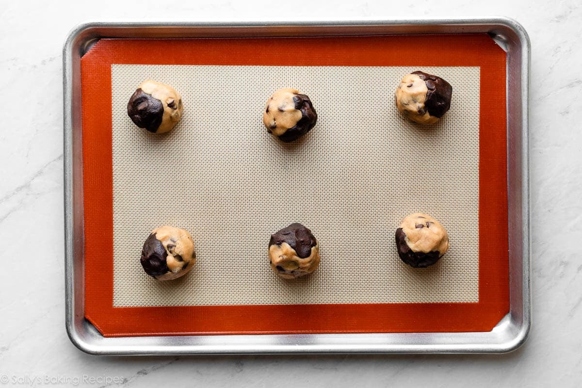 silicone baking mat-lined baking sheet with peanut butter chocolate cookie dough balls on top.