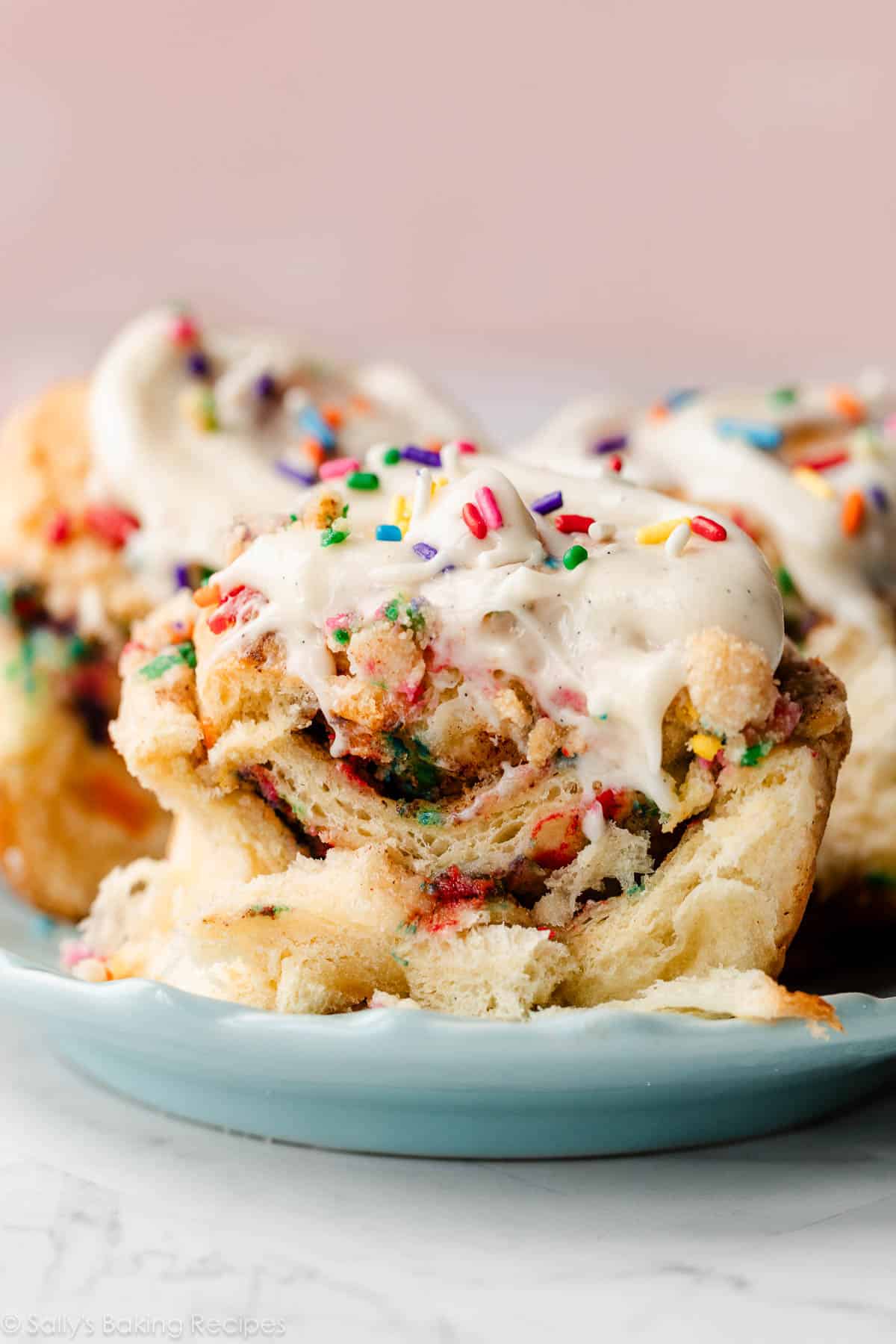 birthday funfetti cinnamon roll cut in half on blue plate with pink background.