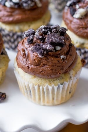 cookies and cream cupcakes topped with chocolate frosting and crushed Oreos on a white dessert stand