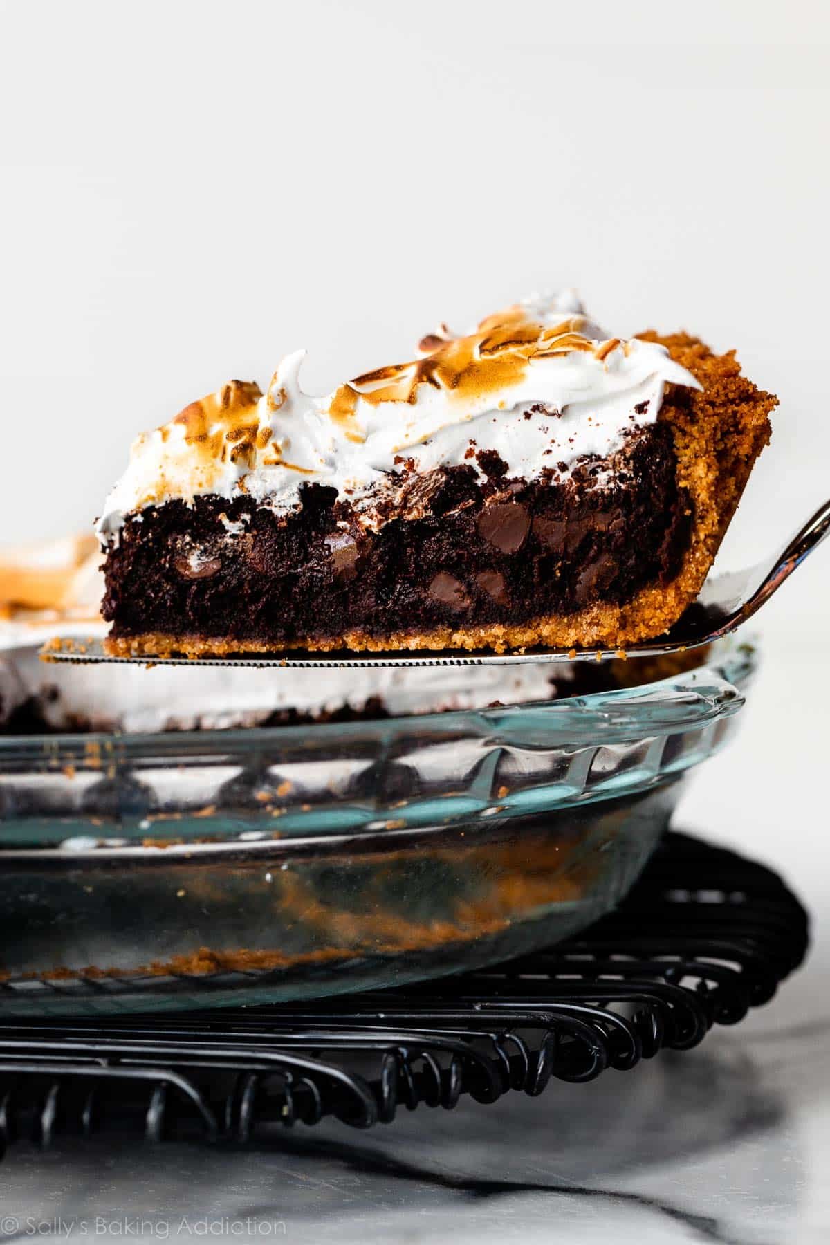 pulling slice of marshmallow meringue topped s'mores brownie pie out of pie dish.