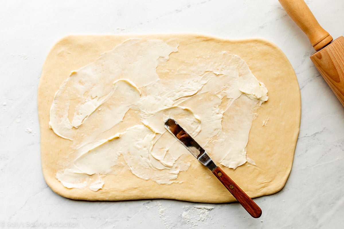 rolled out rectangle shape of dough on counter and butter being spread on top.