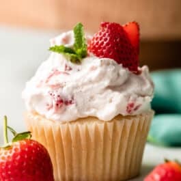 close-up of strawberry shortcake cupcake with whipped cream, mint, and fresh strawberry slices on top.