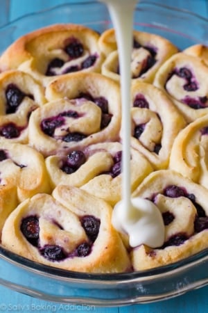 pouring lemon glaze onto blueberry sweet rolls