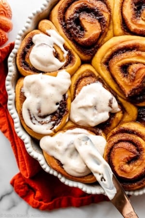 spreading icing on warm pumpkin cinnamon rolls