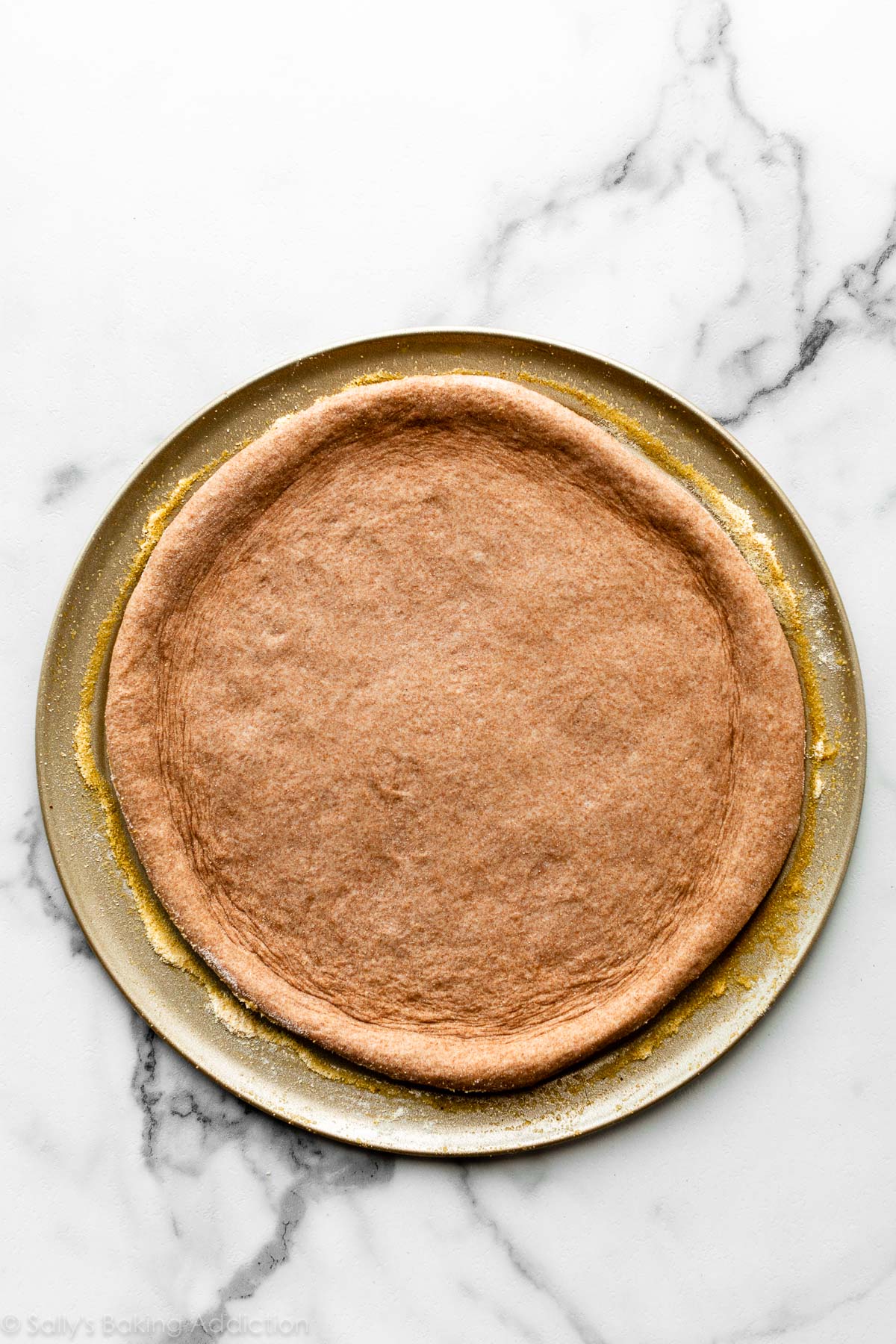 whole wheat pizza dough shaped on pizza pan