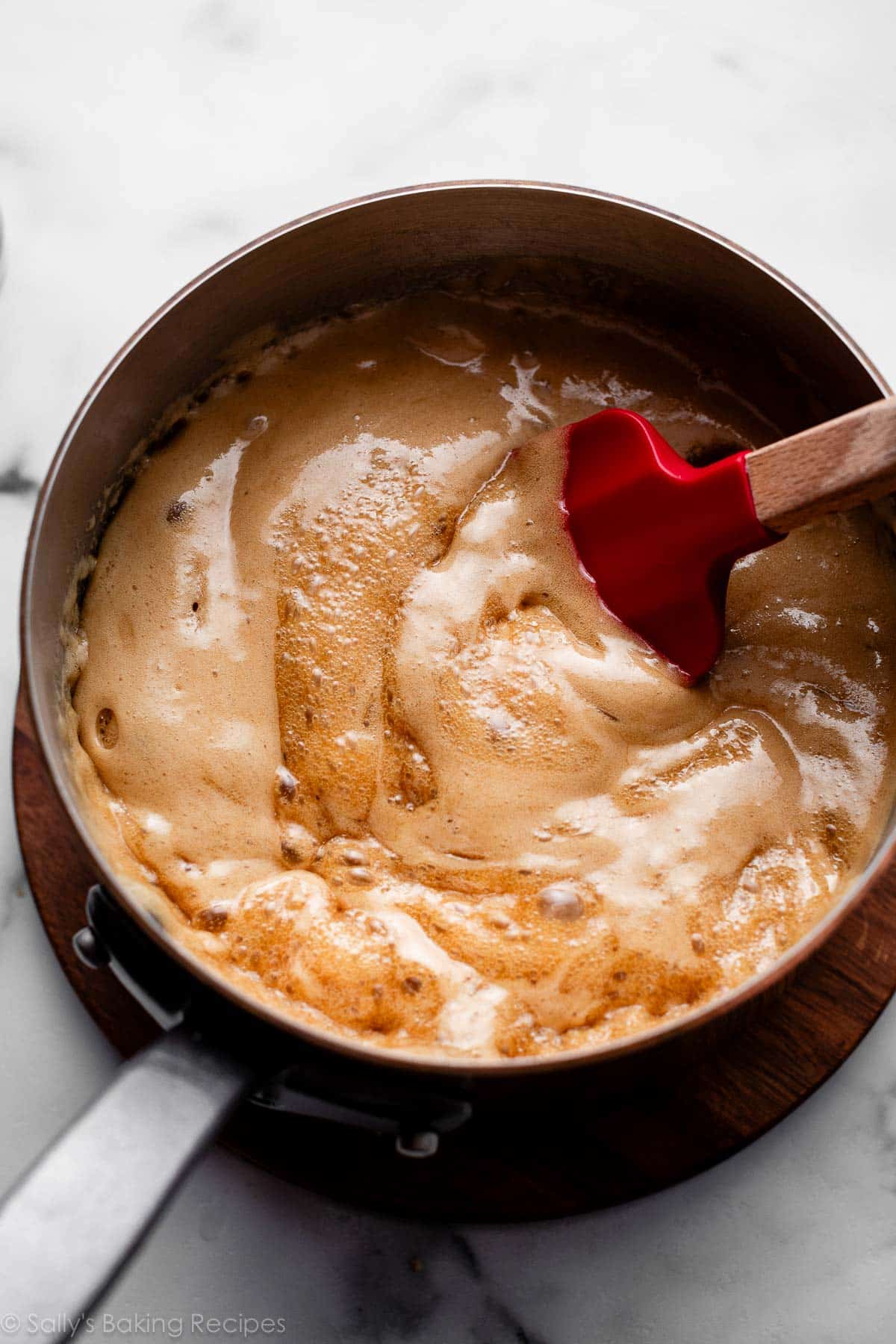 frothy sauce mixture in pot with red spatula.