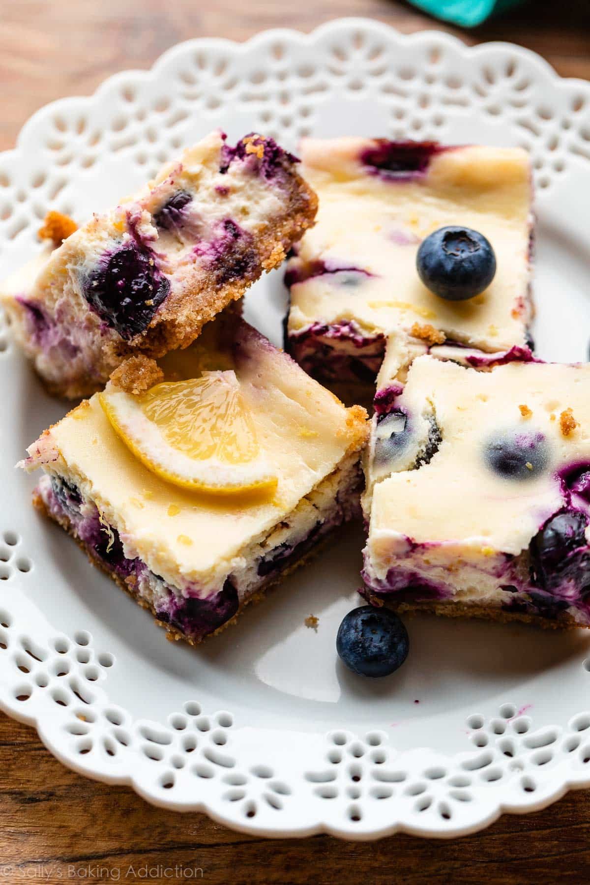 4 lemon blueberry cheesecake bars arranged on white plate.