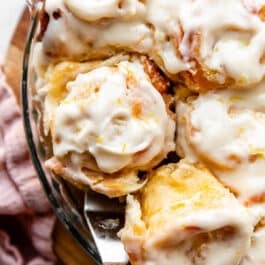 spatula removing a lemon sweet roll with cream cheese icing from the pan.