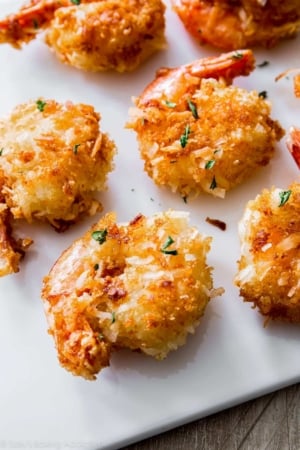 close-up of 6 coconut shrimp on white cutting board.