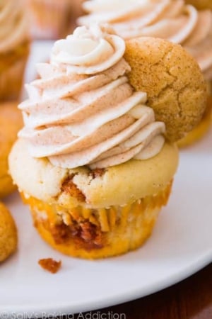 snickerdoodle cupcakes topped with cinnamon and vanilla frosting on a white plate