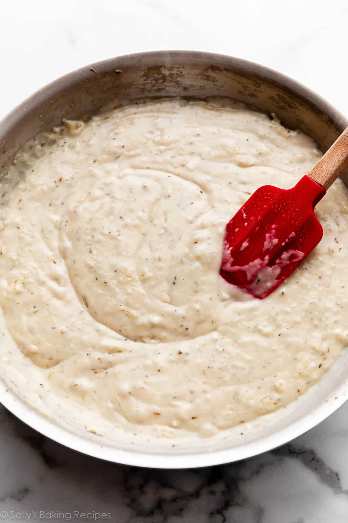 thick white gravy with black pepper specks in skillet with red spatula.