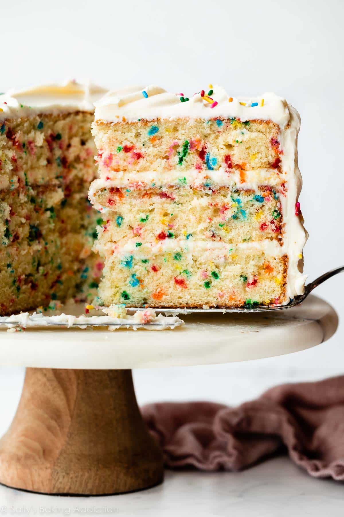 slice of confetti birthday cake being removed from marble cake stand.