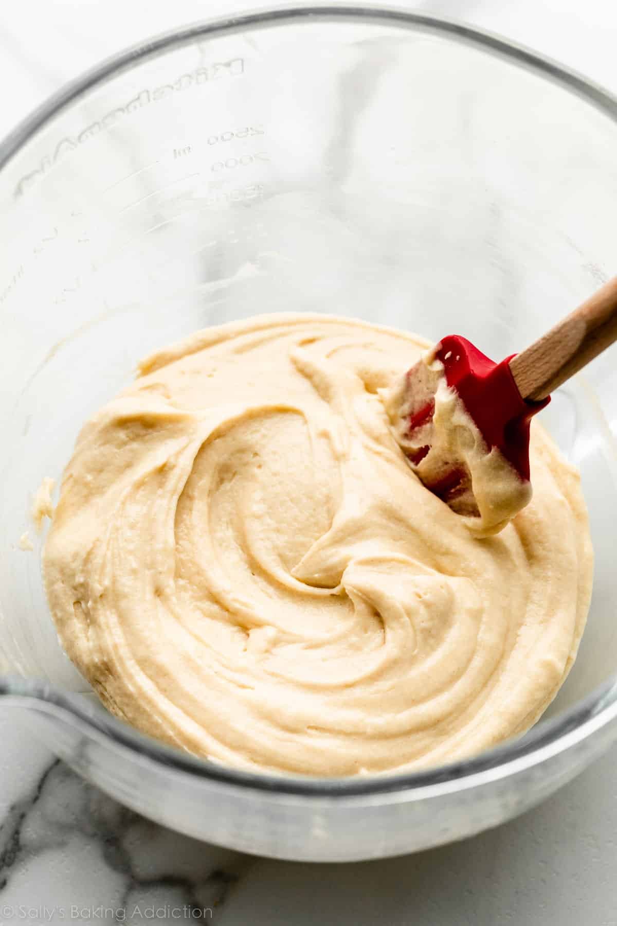 glass bowl of vanilla yellow batter with red spatula.