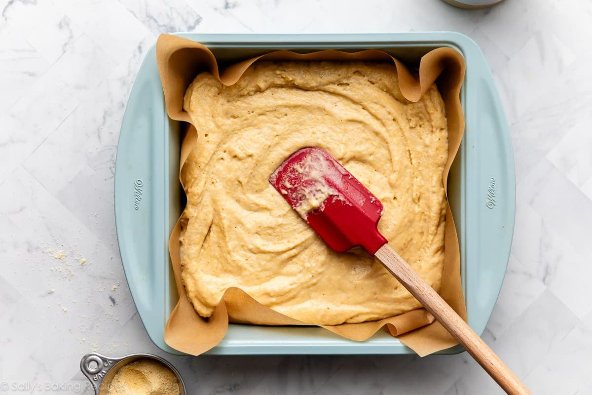 spreading yellow batter into lined blue square baking pan.=