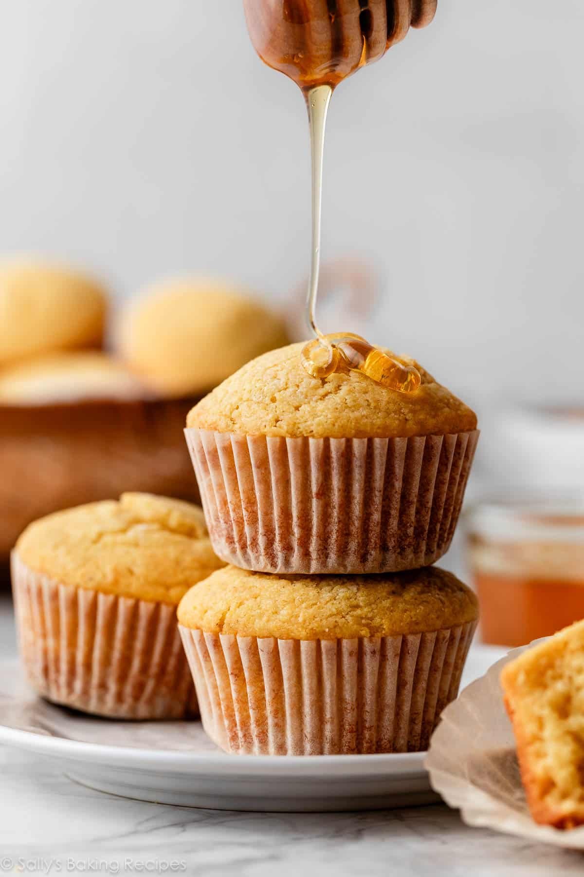 stack of 2 cornbread muffins with honey being drizzled on top.