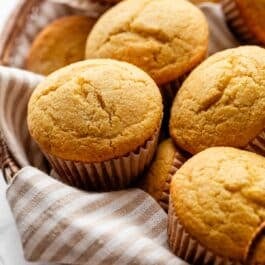 basket of cornbread muffins with beige striped linen.