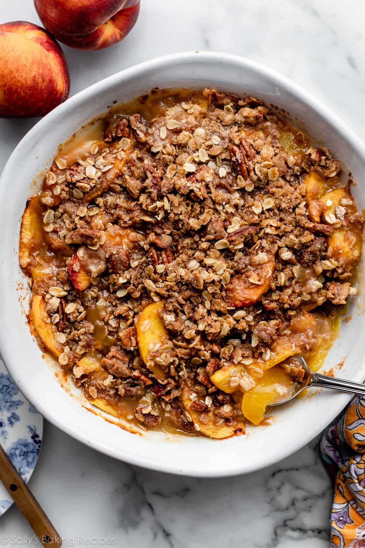 peaches dessert with oat streusel pecan topping in white round baking dish.