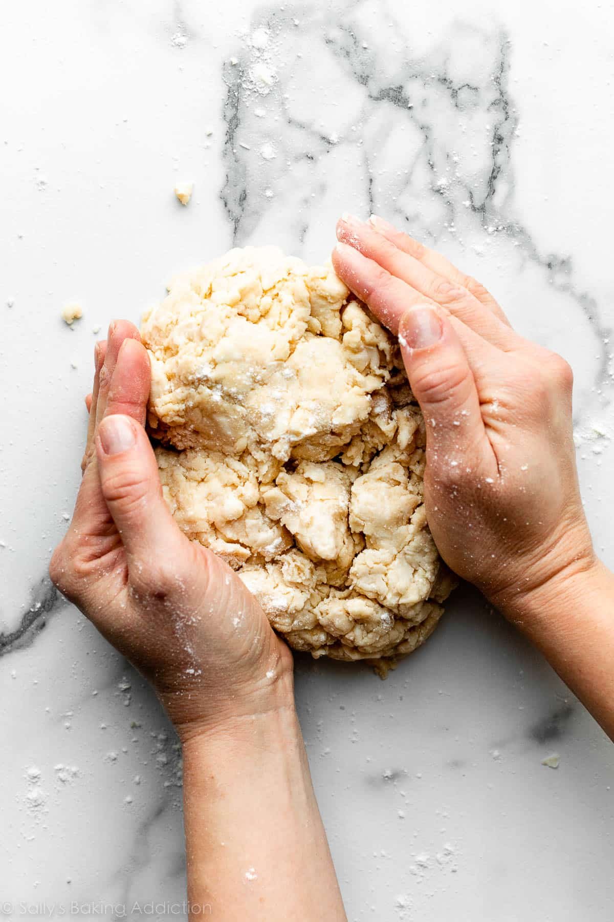 hands forming dough into a circle shape on a marble countertop.