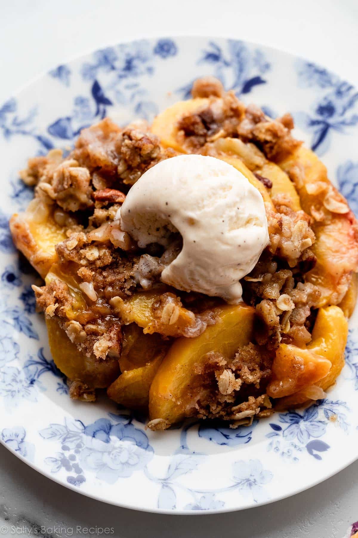 peach crisp with vanilla ice cream on blue floral plate.