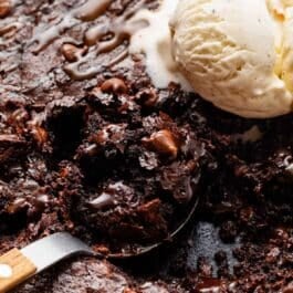 spoonful of brownie out of a cast iron skillet with vanilla ice cream.