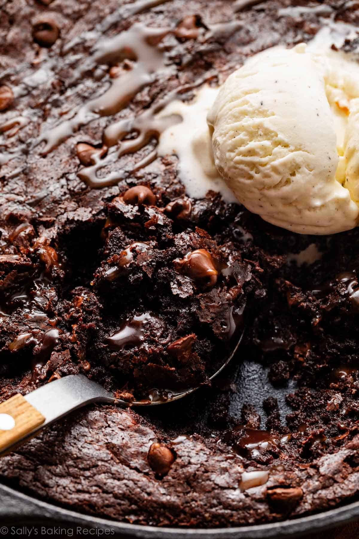 spoonful of brownie out of a cast iron skillet with vanilla ice cream.