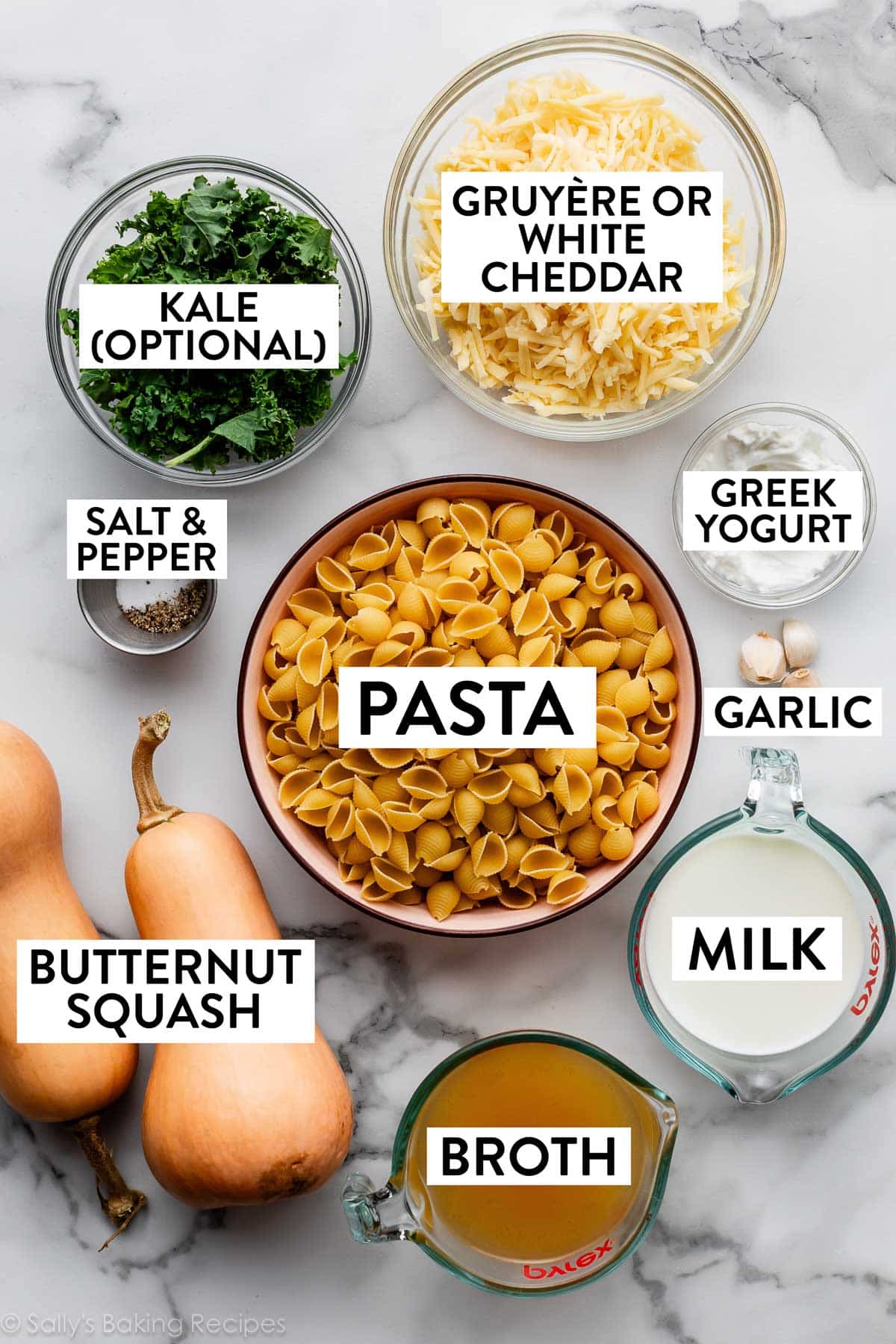 ingredients on marble countertop including pasta, kale, gruyere cheese, greek yogurt, milk, broth, and garlic.