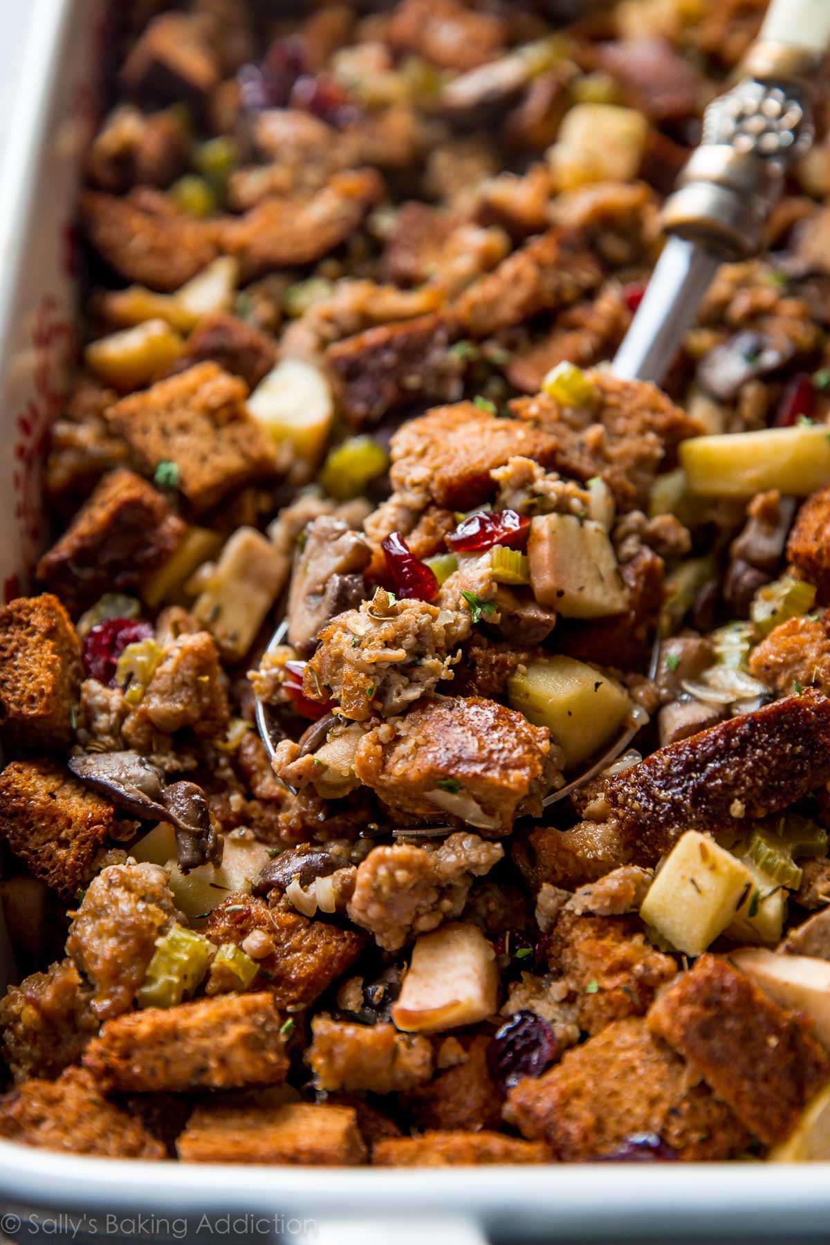 herbed sausage and apple stuffing in a white baking dish with a serving spoon