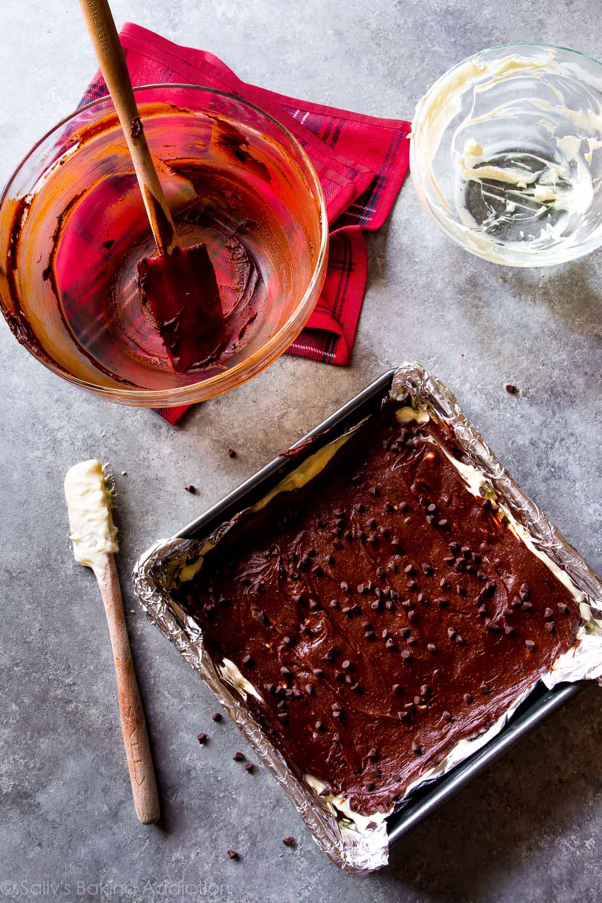 mocha cheesecake brownies in a baking pan before baking with empty glass bowls