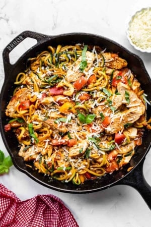 bruschetta tomatoes and cooked sliced chicken over zucchini noodles with fresh basil garnish in cast iron skillet.