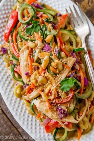 peanut chicken zucchini noodles on a white serving tray with a fork