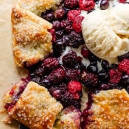 sliced mixed berry galette with melted vanilla ice cream on top.