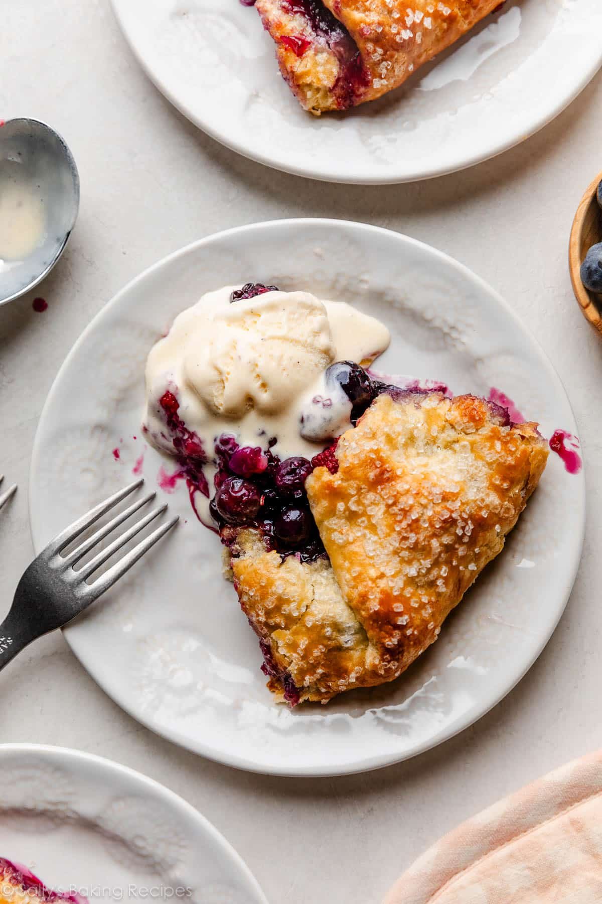 slice of berry galette on white plate with melted vanilla ice cream on top.