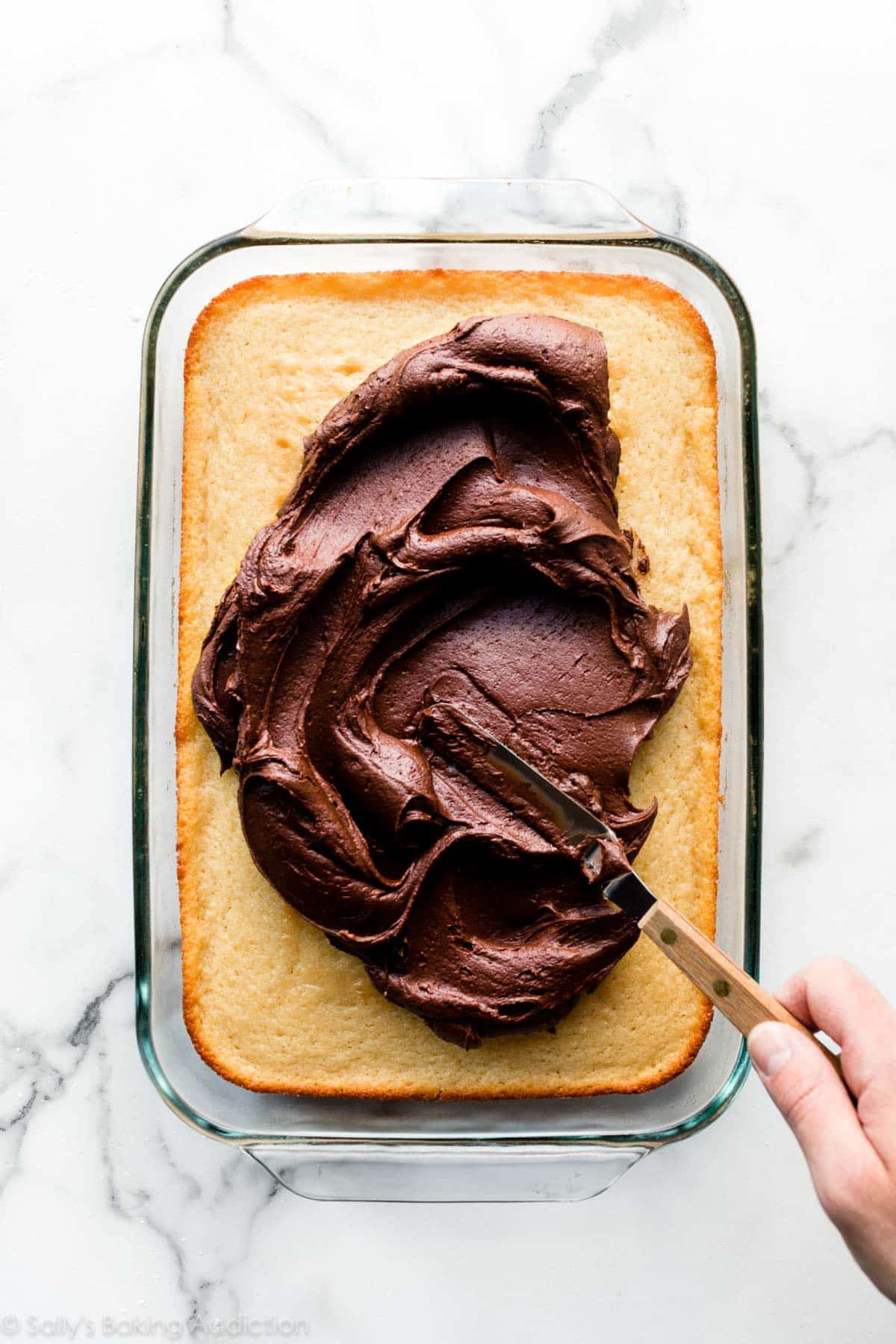 spreading chocolate frosting on a yellow sheet cake