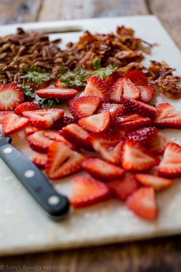 sliced strawberries and chopped bacon on a white cutting board