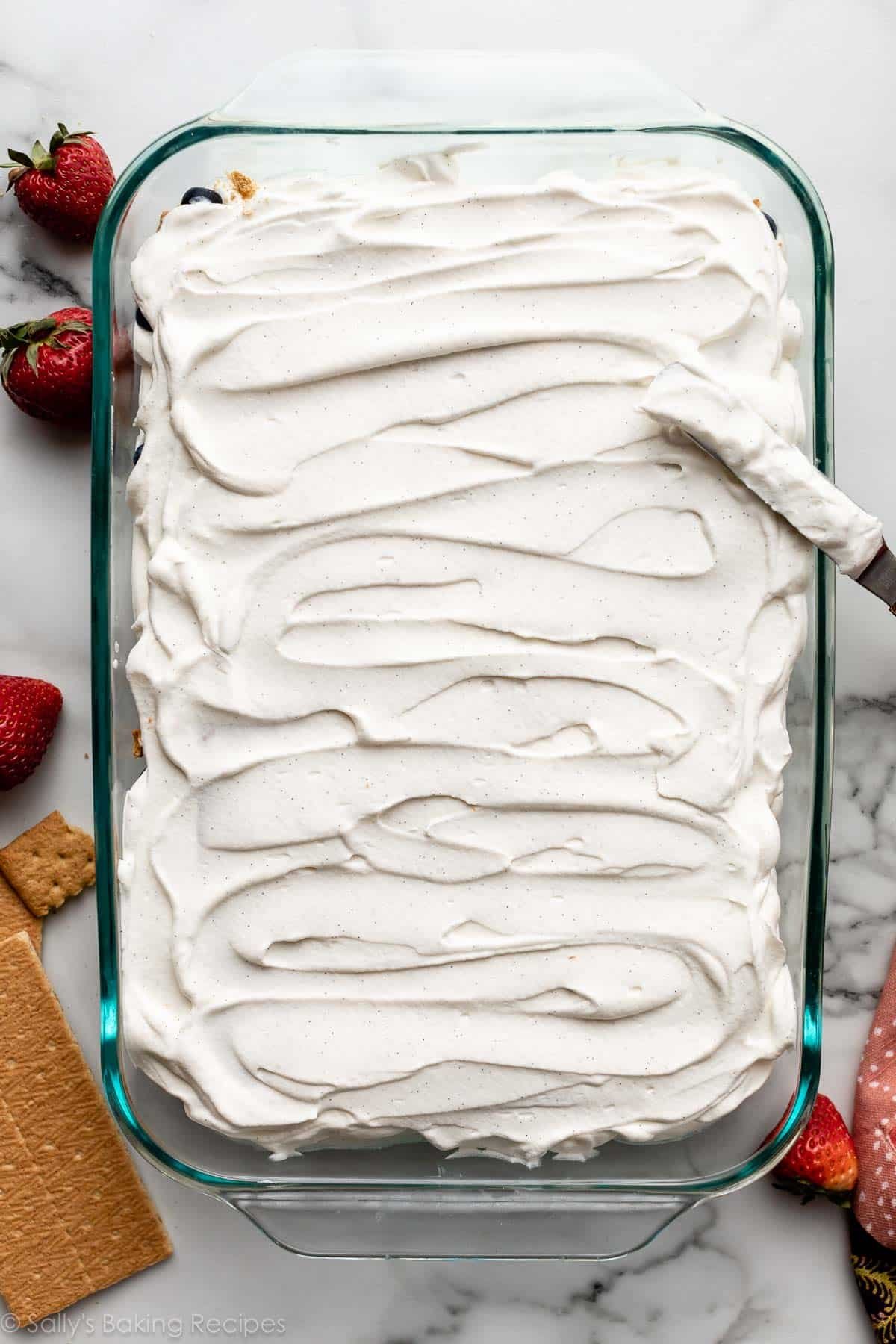 spreading whipped cream on top of cake in glass pan.