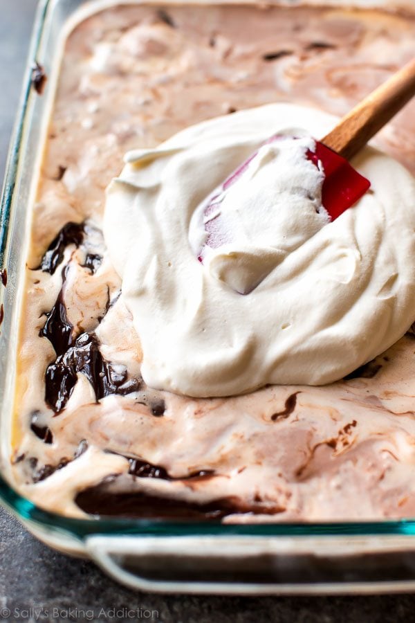 spreading whipped cream layer of ice cream cake into glass baking dish