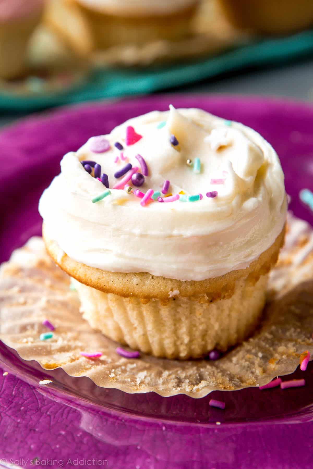 Vanilla cupcake with vanilla frosting and sprinkles on a purple plate