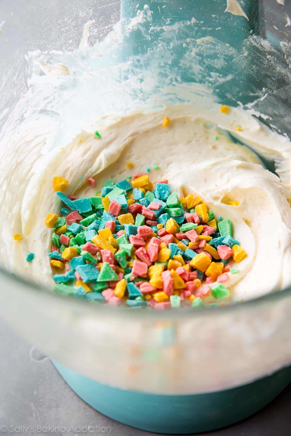 rainbow chips added to frosting in a glass bowl