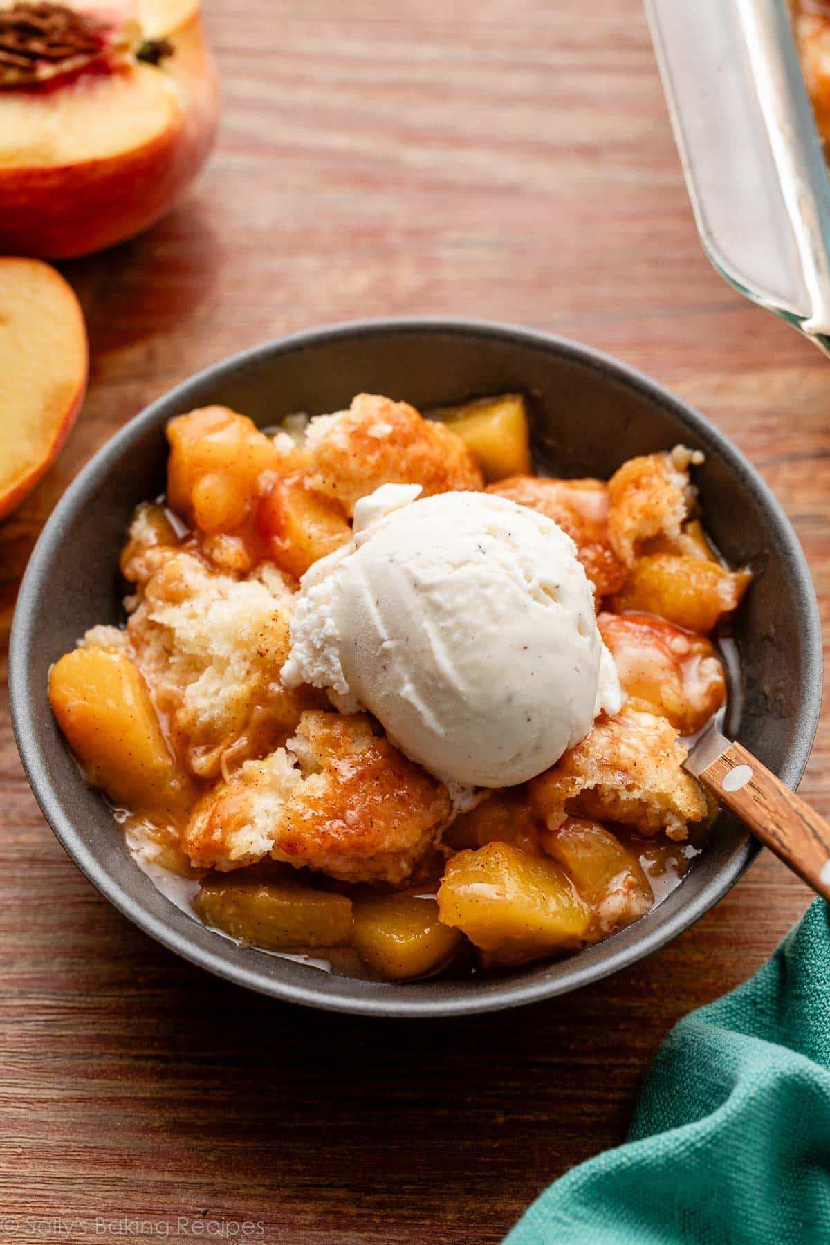 peach cobbler with biscuit topping and vanilla ice cream in gray bowl on wooden backdrop.