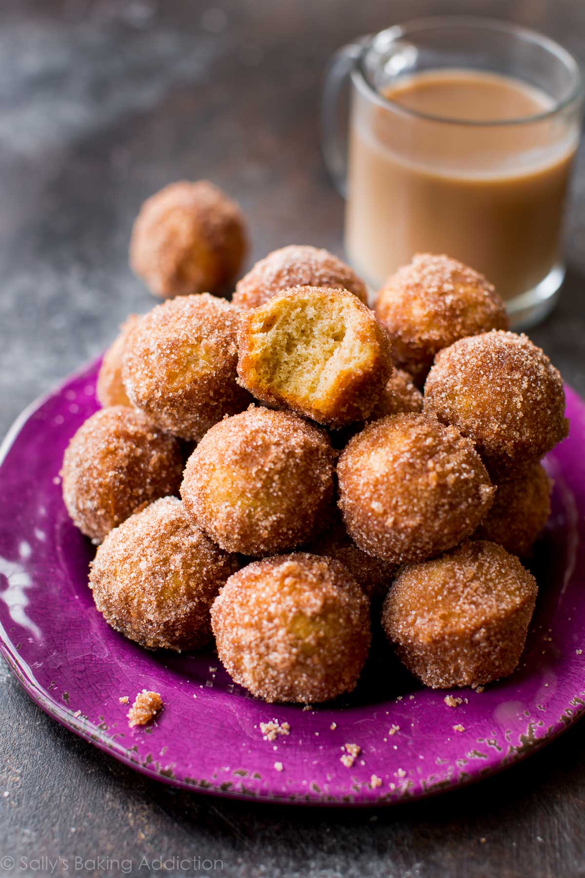 chai spice donut holes on a purple plate with a cup of coffee in a glass mug